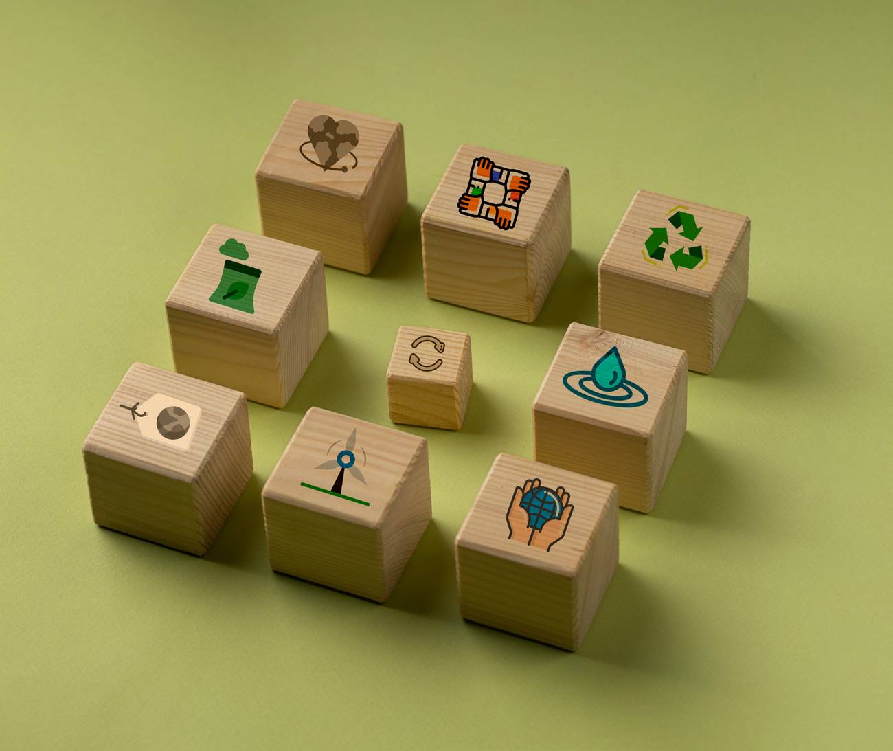 Wooden cubes printed with sustainability icons scattered across an olive-green surface.